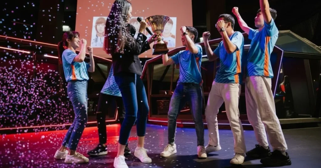 Esports team in blue jerseys celebrates on stage with a trophy and falling confetti.