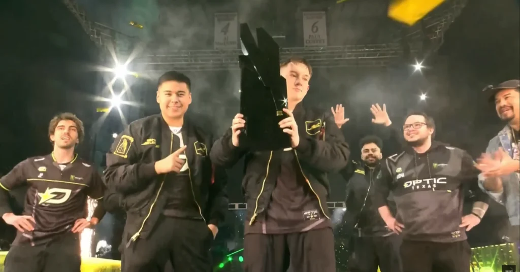 OpTic Texas players celebrate on stage with a black trophy, fireworks, and sponsor-branded jerseys.